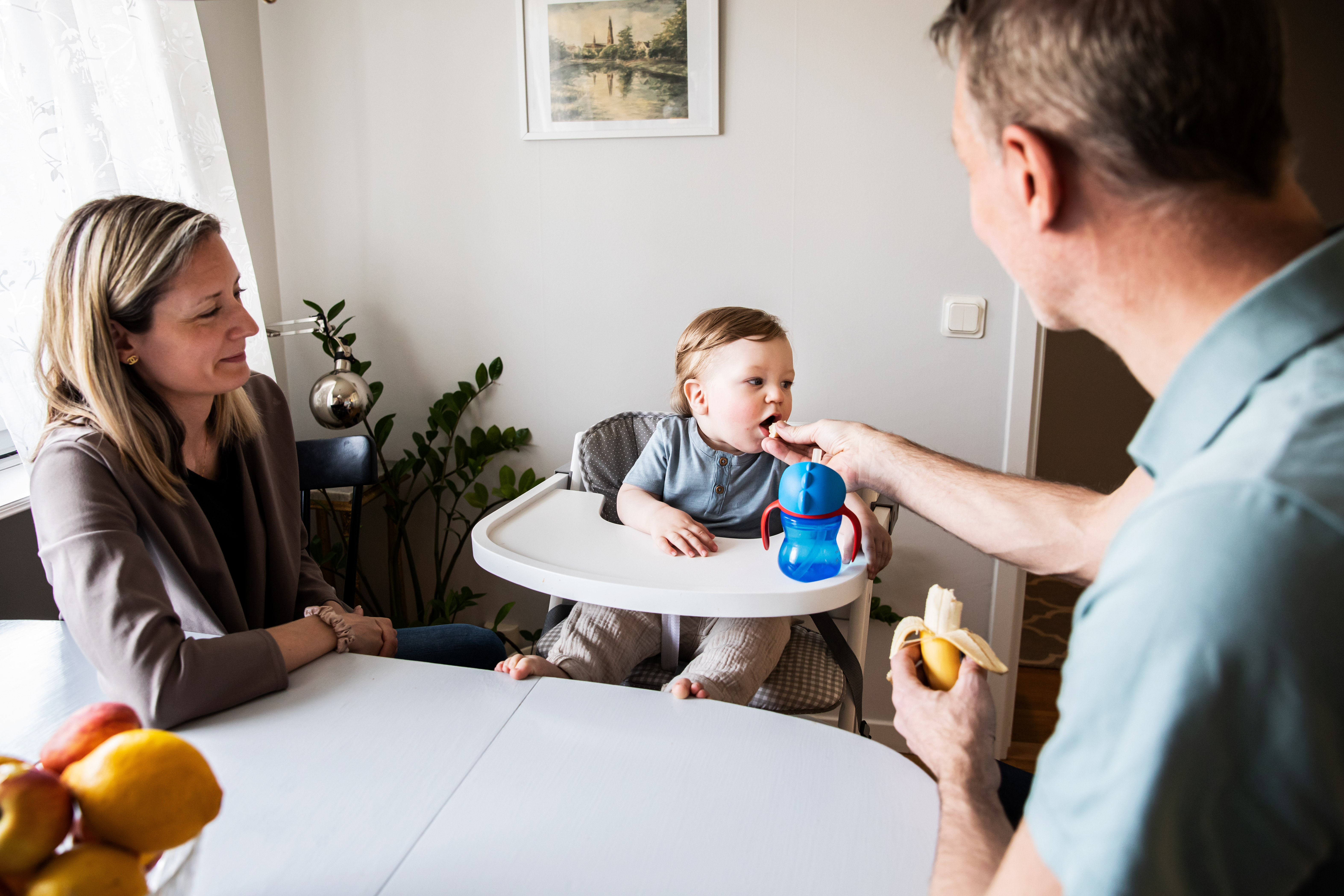 Litet barn sitter med vid matbordet tillsammans med två vuxna